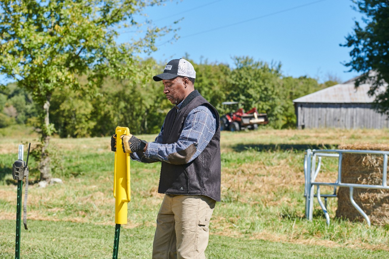 Image of a person using a post driver in a field.