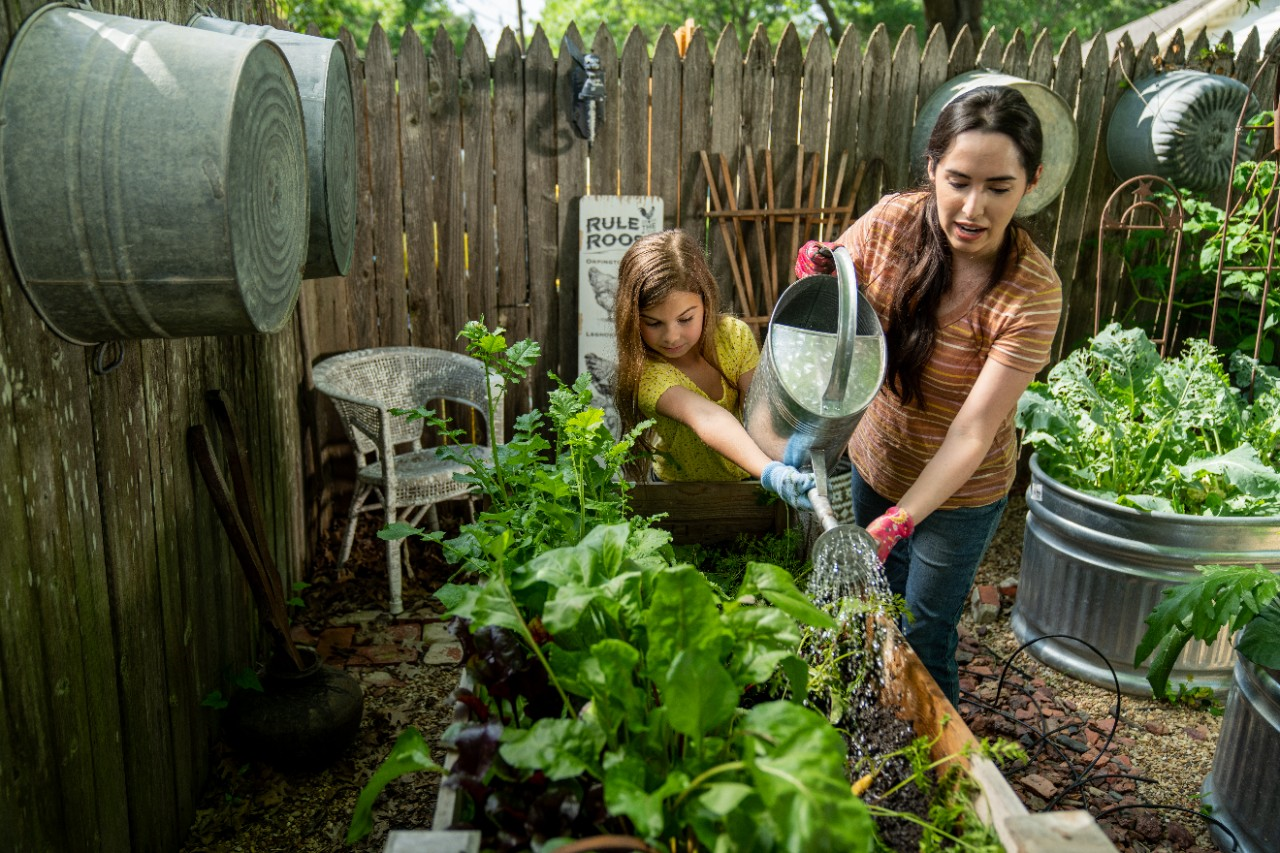 Image of a woman and child watering a patio garden container.