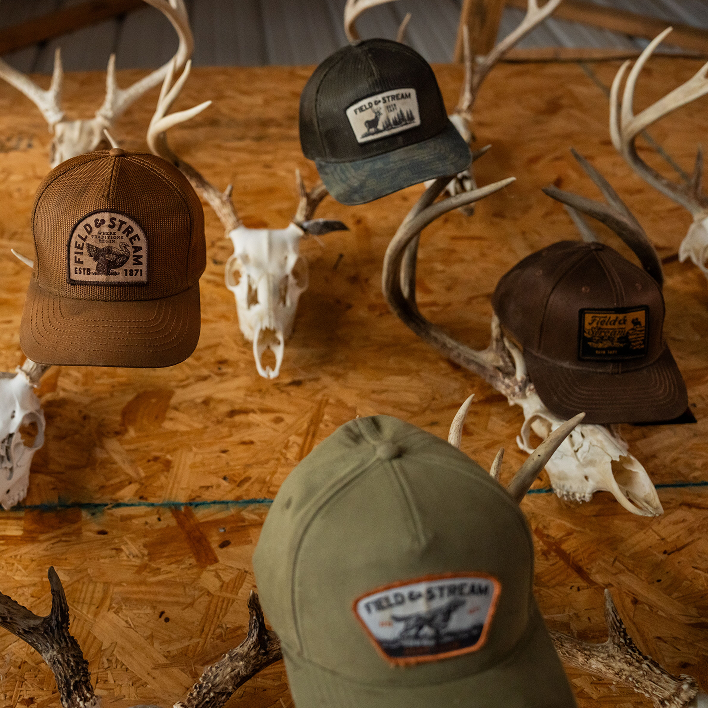 A table with 4 Field and Stream baseball caps in different colors interspersed with small animal skull decor. See and shop items.