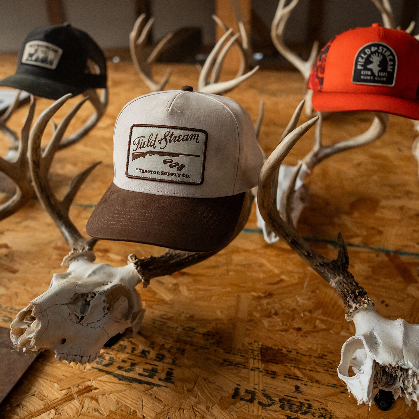 A table with 3 Field and Stream baseball caps in different colors interspersed with small animal skull decor. See and shop items.