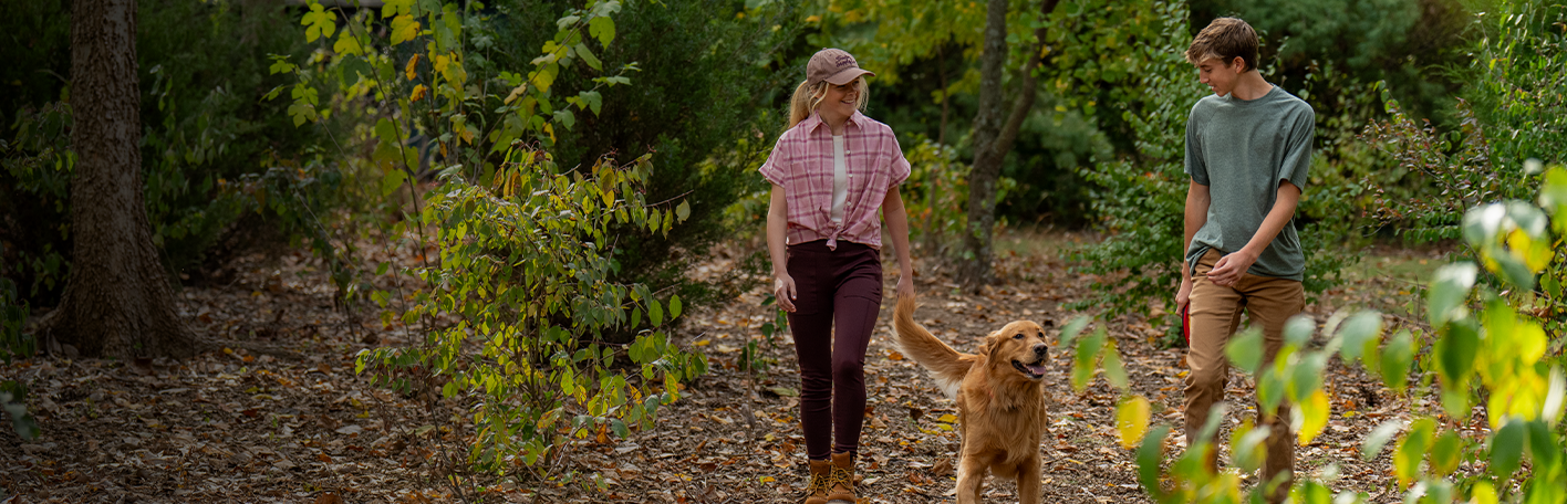 Flea and tick prevention banner with text, Must-haves to keep your pet pest-free, featuring two people walking a dog. Shop now. 