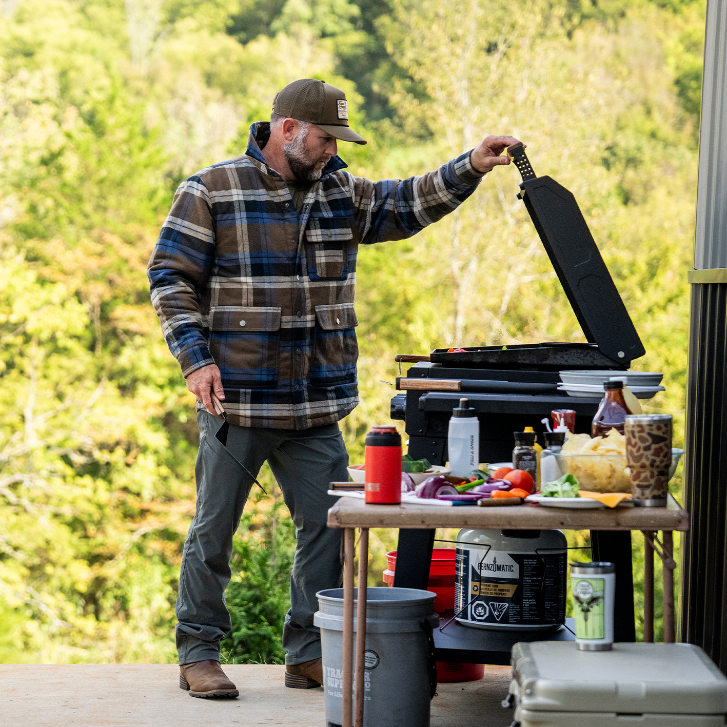 A man wearing a plaid jacket is shown grilling outdoors. See items.
