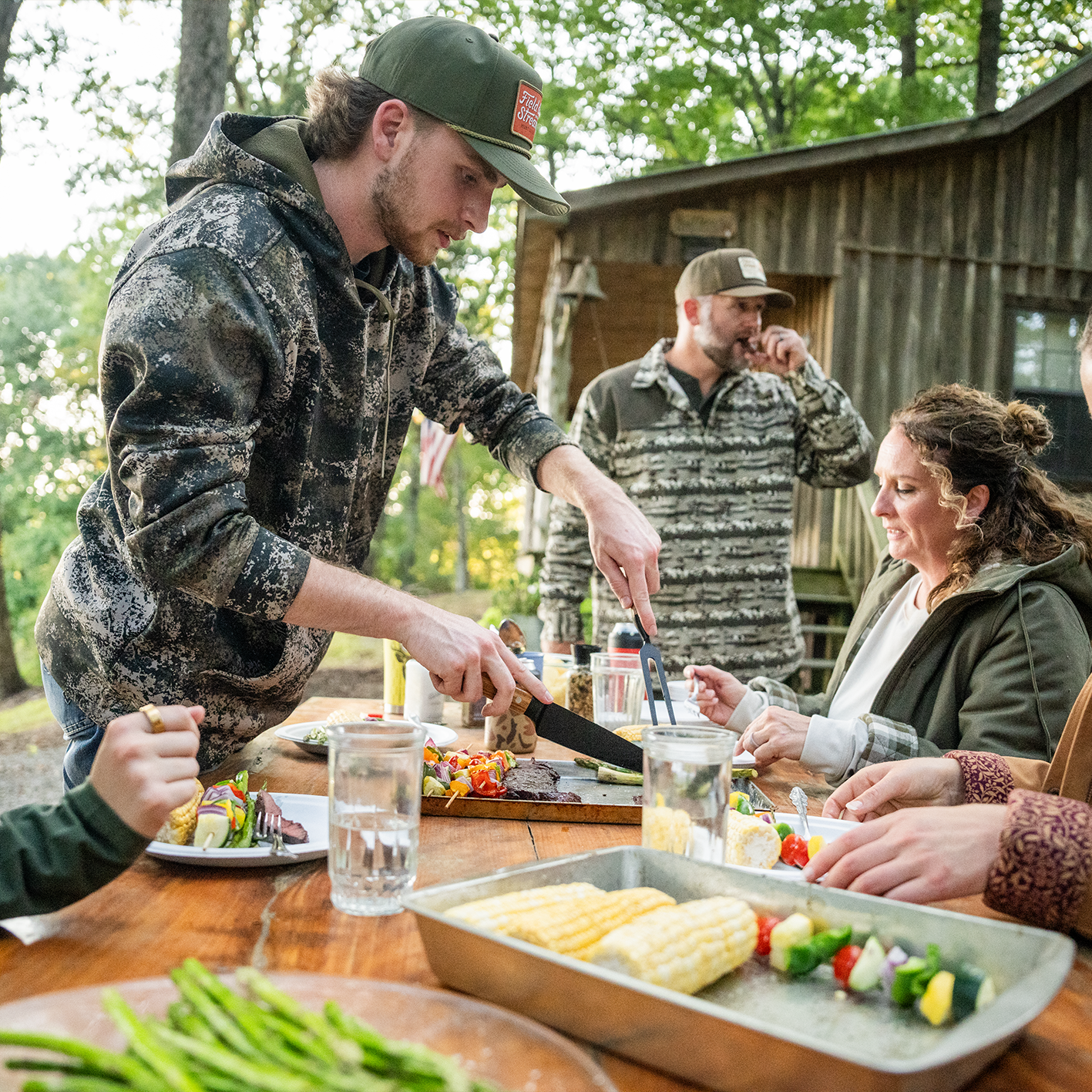 People wearing outdoor apparel are shown preparing food at a picnic table. See items.