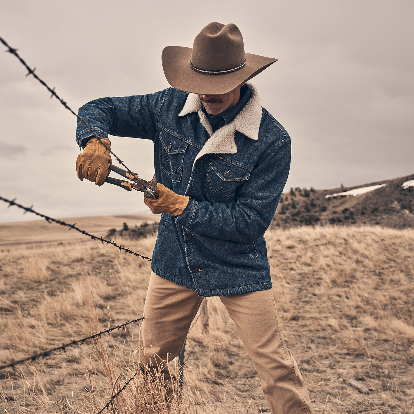 Man fixing barbed wire fence with cowboy hat and sherpa lined denim coat