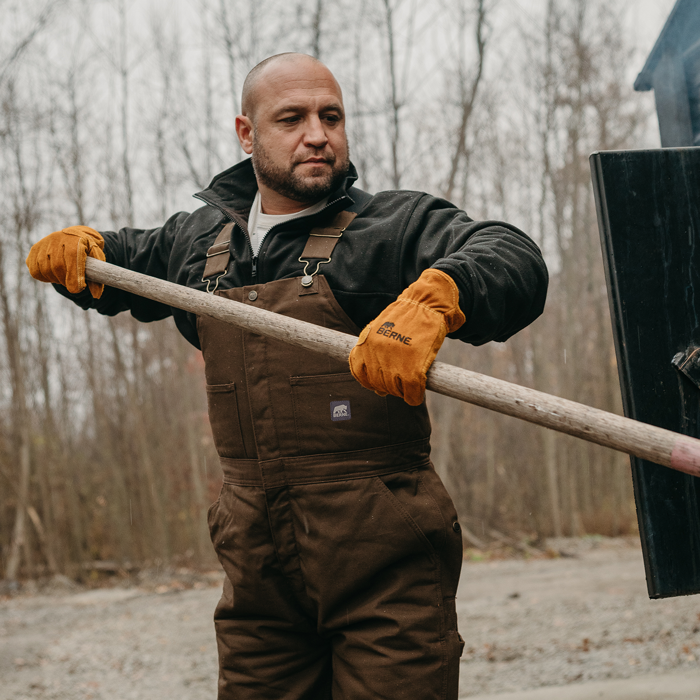 Man in coveralls and leather gloves holding long handled tool. See and shop items. 