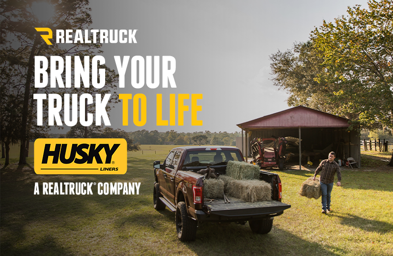  A banner with a sunny outdoor scene with a man carrying a load of hay to a truck with the text, realtruck, bring your truck to life.     