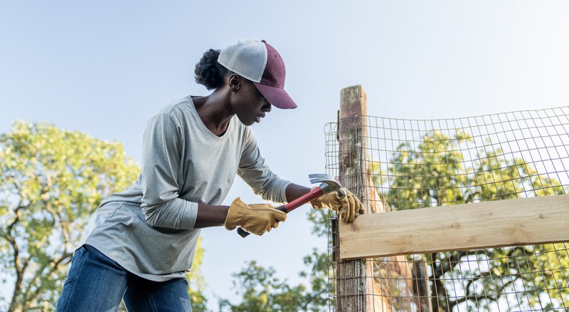 Woman using hammer and nail to secure wood board to fence post
