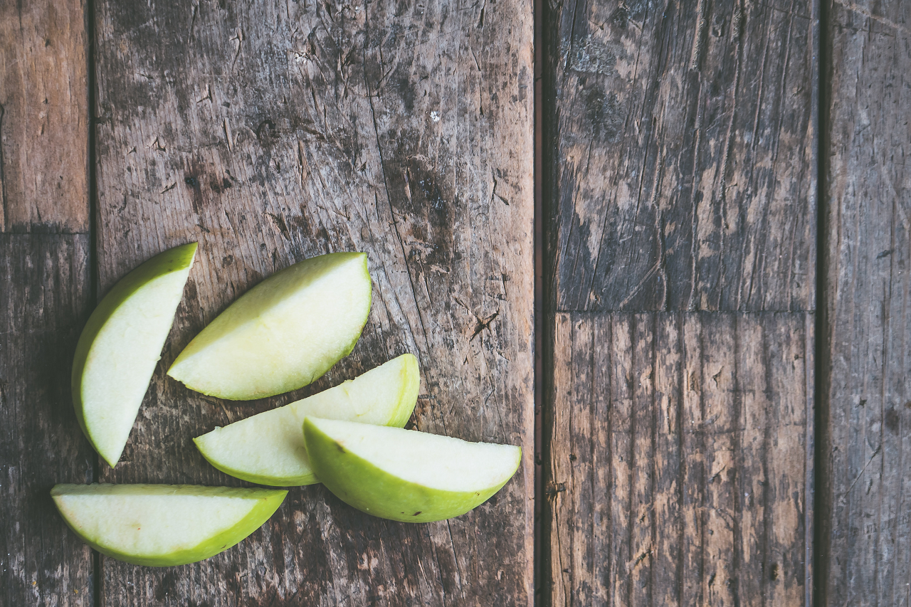 Image of a green apple sliced up on a wooden table.