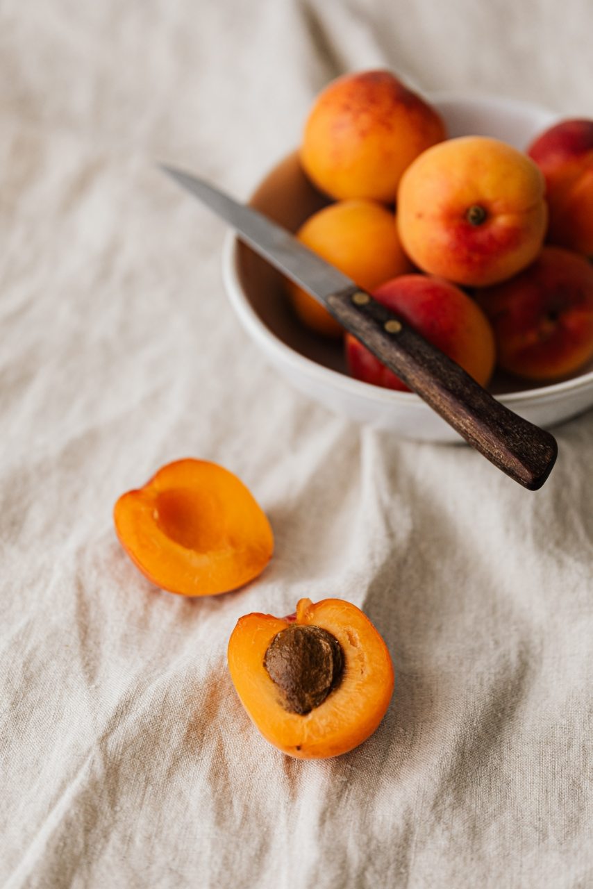 Image of a fresh peach cut in half next to a bowl of peaches.