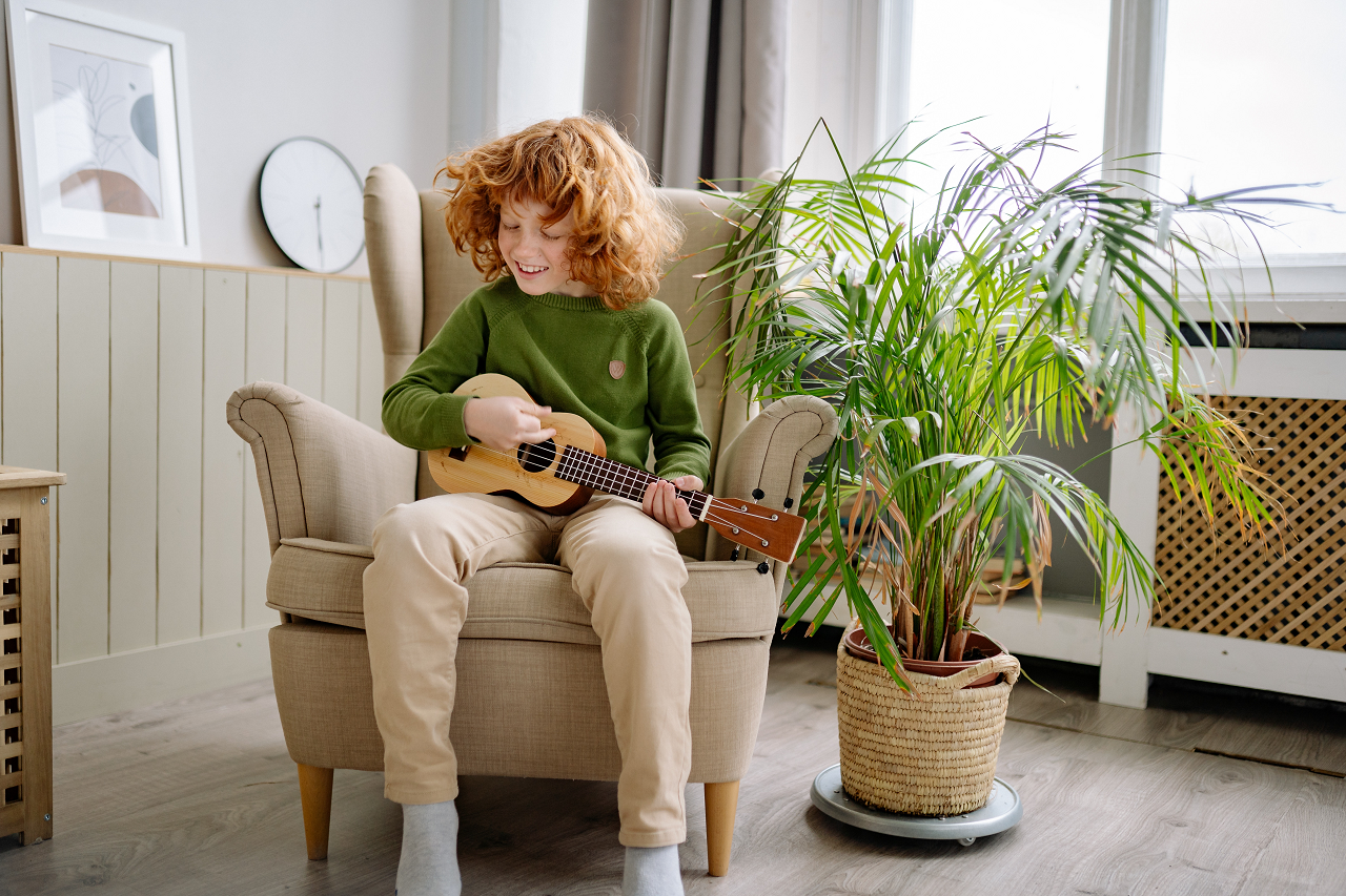 Image of a kid playing an instrument next to a fern.