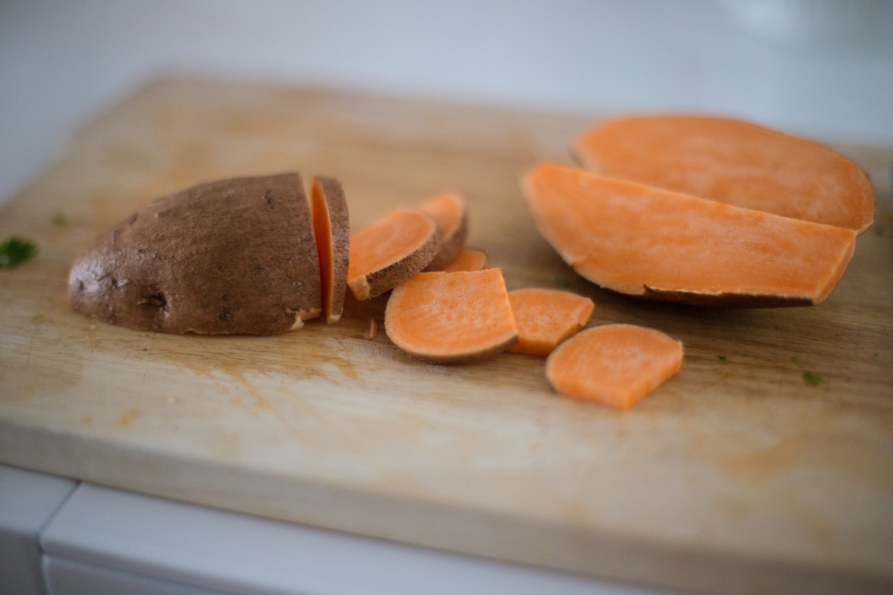 Image of sweet potato chopped up on wooden cutting board.