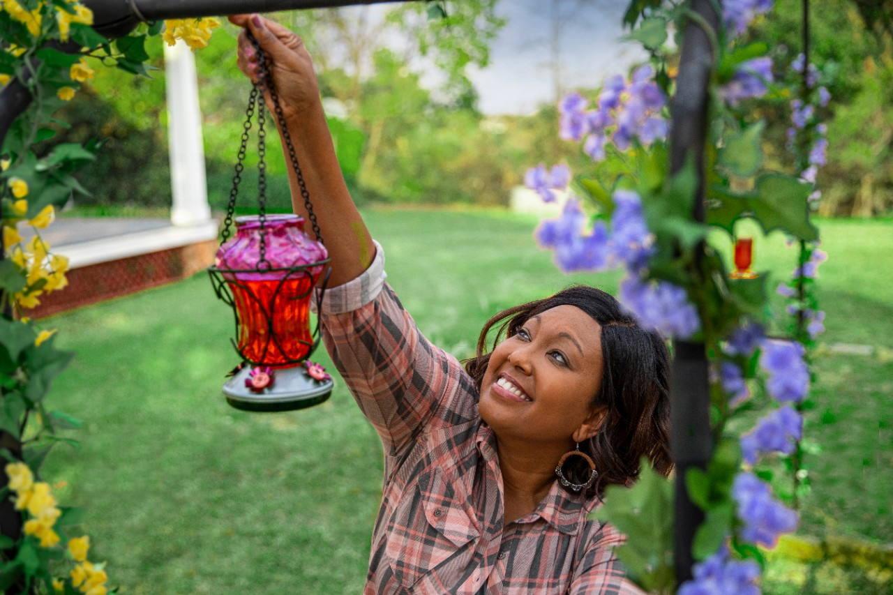 Image of a person hanging a hummingbird feeder near flowers.