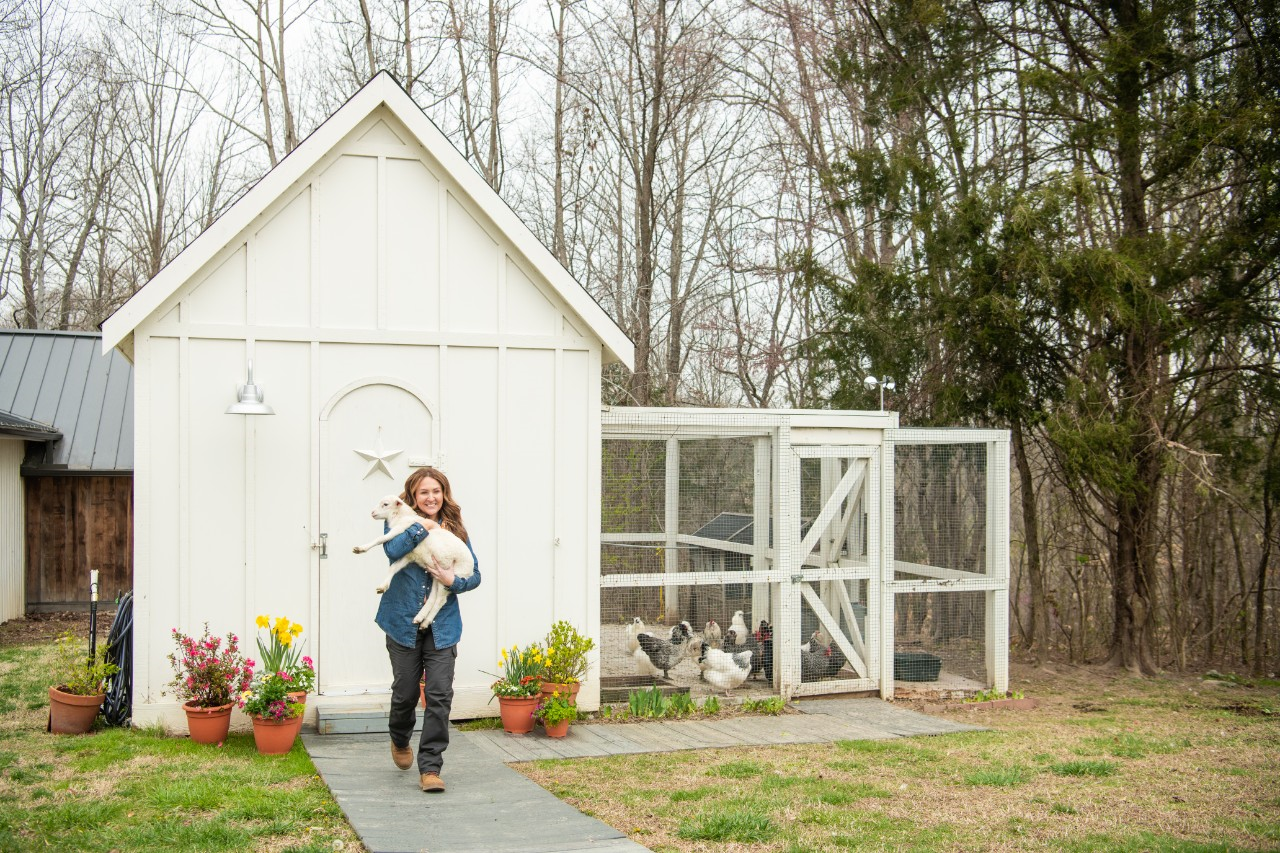Image of a person carrying a lamb in front of a chicken coop.