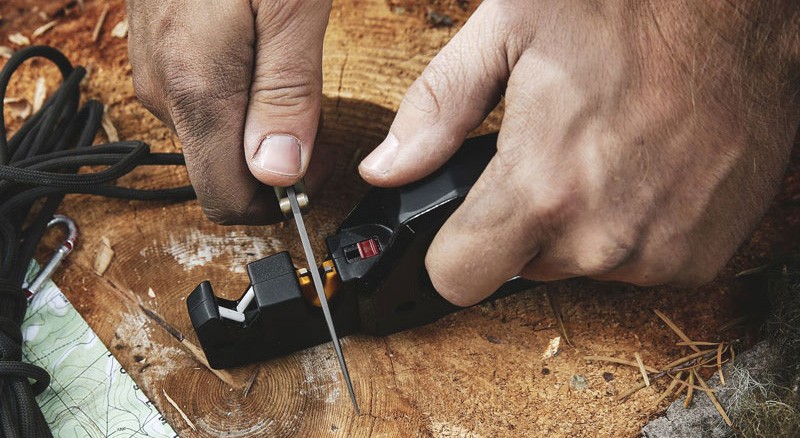 Person using knife sharpener to sharpen blade at camp site